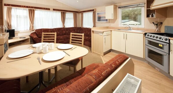 A compact RV interior with a dining area, kitchenette, and a window. - Sandy Glade Holiday Park (Burnham-on-Sea)