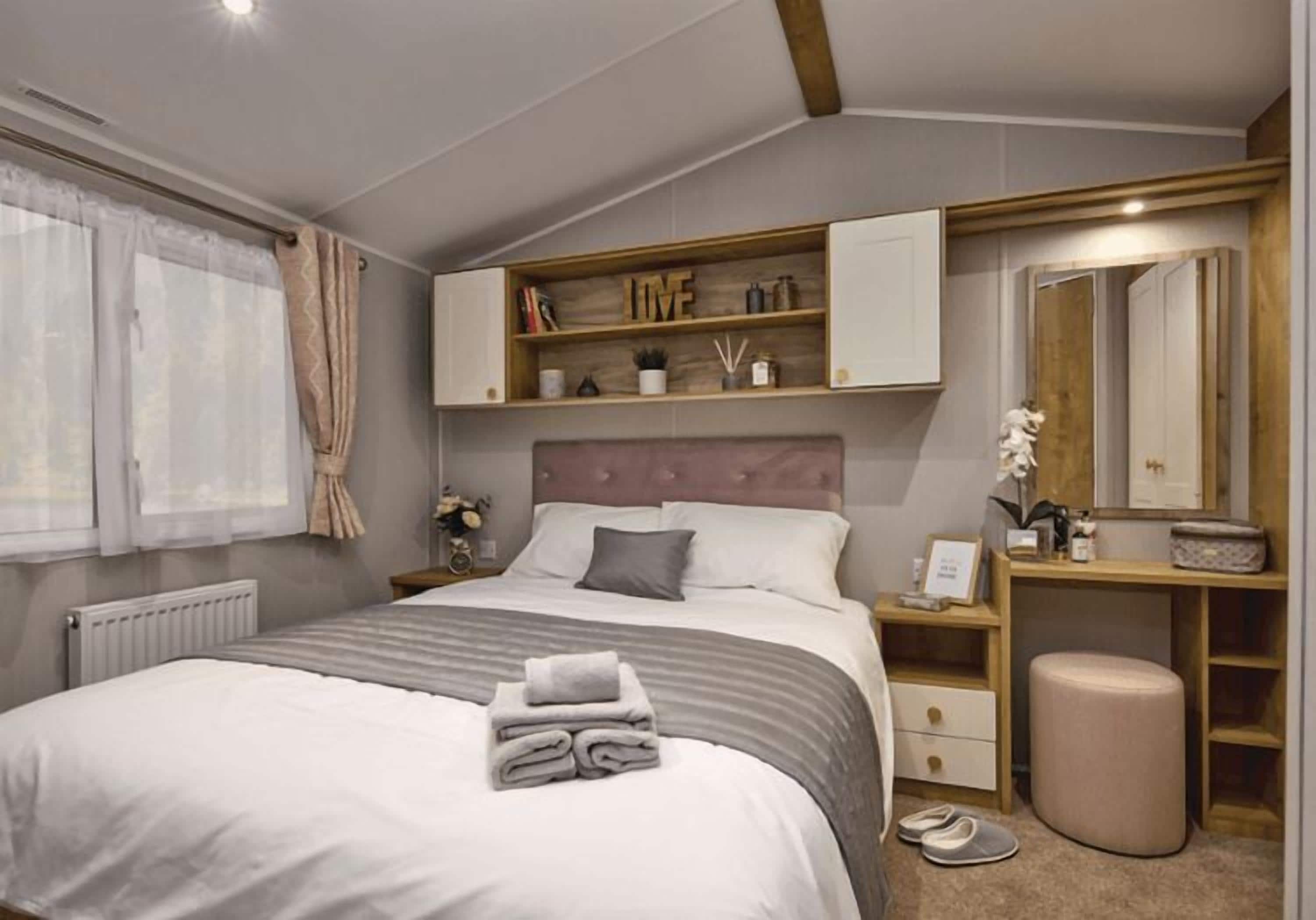 A bedroom with a bed, bedside tables, a wardrobe, a mirror, and a window with curtains.