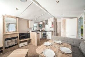 A compact living space with a kitchenette, a dining area with a table set for two, a sofa, and a television. - Sandy Glade Holiday Park (Burnham-on-Sea)