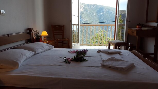 A hotel room with a bed, a chair, a desk, and a balcony with a mountain view. - Epic Rooms (Delphi)