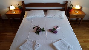 A neatly made bed with white linens, two pillows, and two towels folded at the foot of the bed. There are two bedside tables with lamps and potted plants. - Epic Rooms (Delphi)