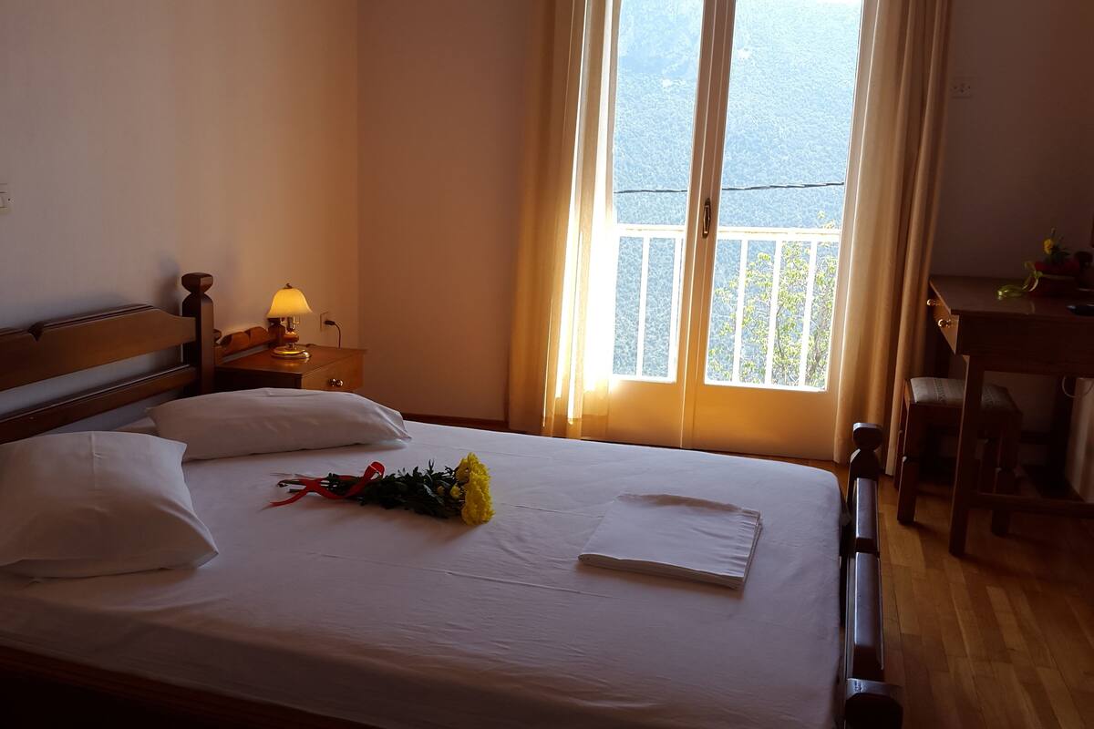 A neatly made bed with white linens, a bedside lamp, and a bouquet of yellow flowers.