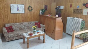 A reception area with a wooden reception desk, a patterned sofa, a small table with a vase of flowers, and a radiator. - Epic Rooms (Delphi)