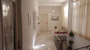 A hallway with a staircase leading to a landing. There are framed pictures on the walls, a door labeled '2', and a window with curtains. - Epic Rooms (Delphi)
