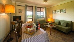 A furnished room with a checkered table set for dining, a green sofa, a television, and a window with curtains. - Borgo Filicardo (Montespertoli)
