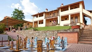 A checkered outdoor area with chess pieces, a building with balconies, and a stone wall. - Borgo Filicardo (Montespertoli)