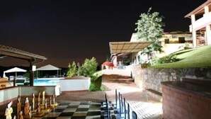 A checkered outdoor area with a pool in the background, a covered seating area, and a building with a sloped roof. - Borgo Filicardo (Montespertoli)