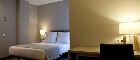 Una habitación de hotel con una cama, una lámpara de noche y un escritorio con una silla.