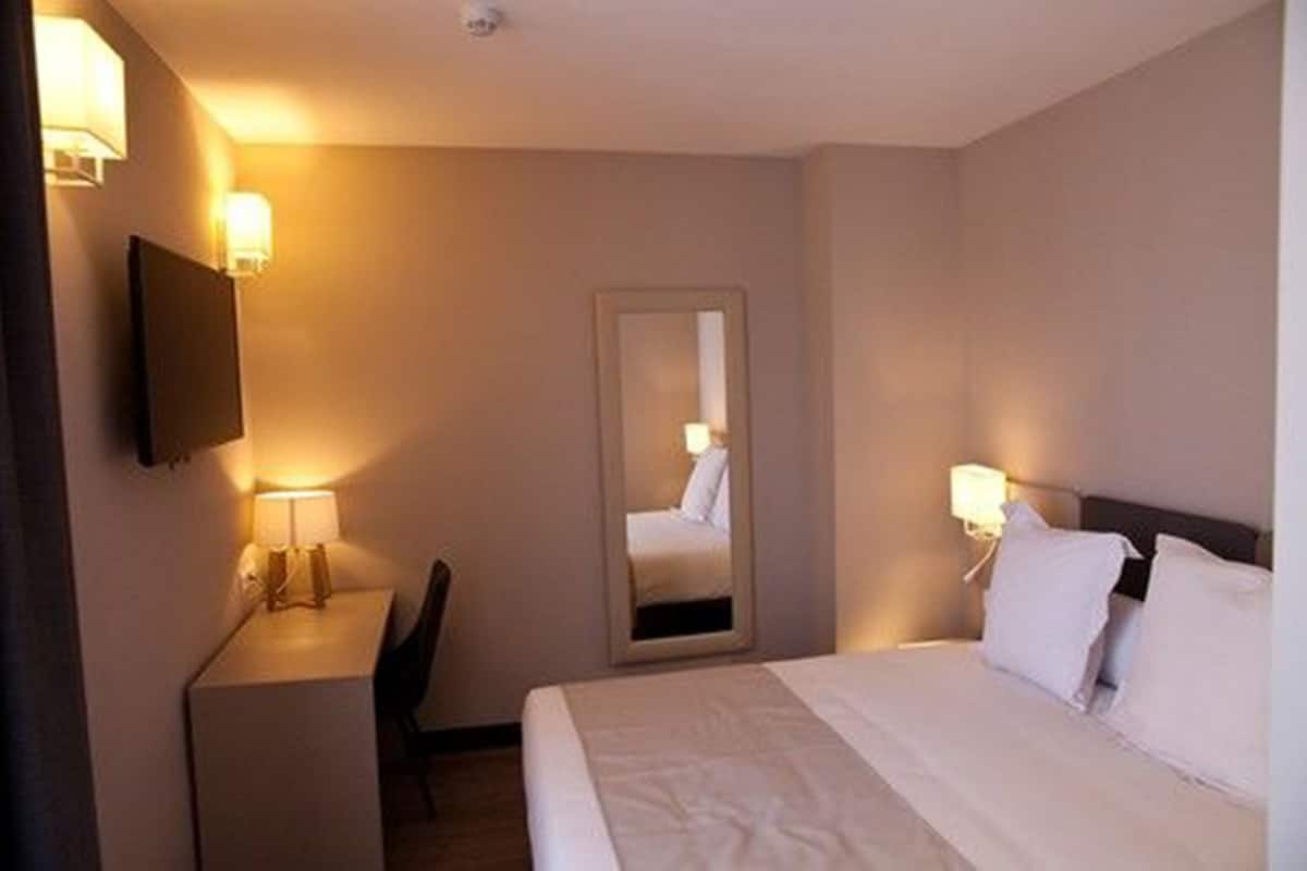 A hotel room with a bed, bedside lamps, a desk with a chair, a flat-screen TV, and a mirror on the wall.