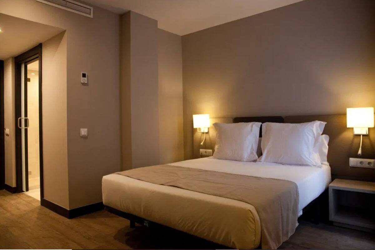 A hotel room with a large bed, two bedside lamps, and a door leading to another room.