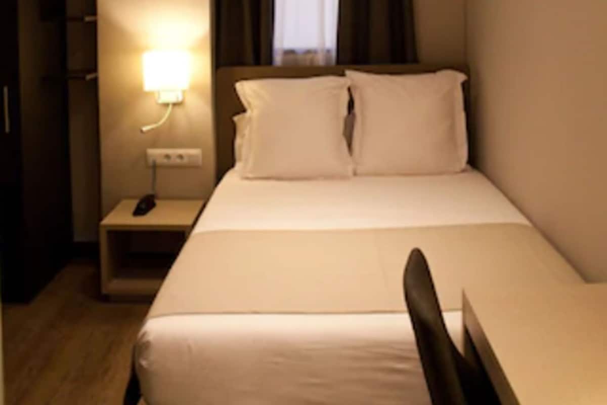 A hotel room with a bed, bedside table, lamp, and a wardrobe.