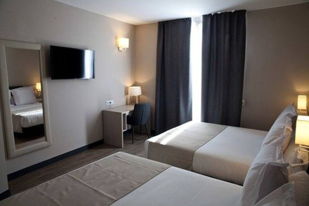 A hotel room with two beds, a desk, a chair, a TV, and a window with curtains.