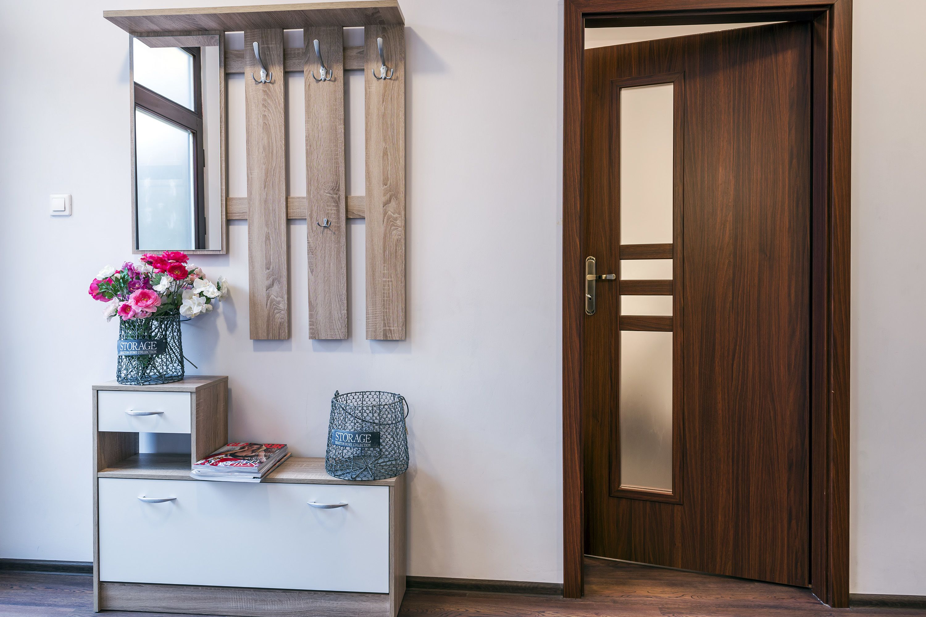 A wooden door, a white console with drawers, a mirror, and a vase with flowers.