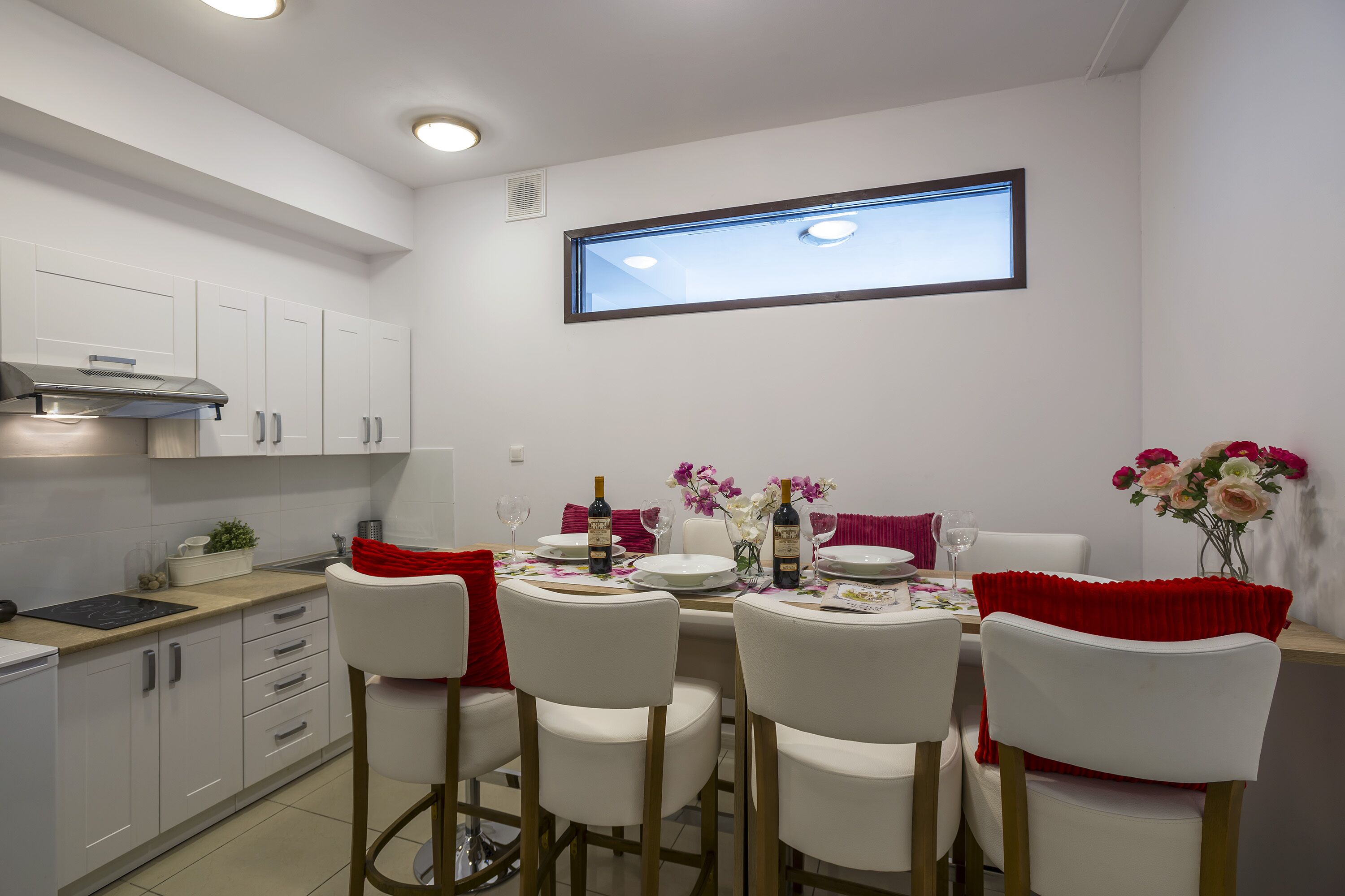 A modern kitchen with white cabinets, a built-in stove, and a window above the dining table.