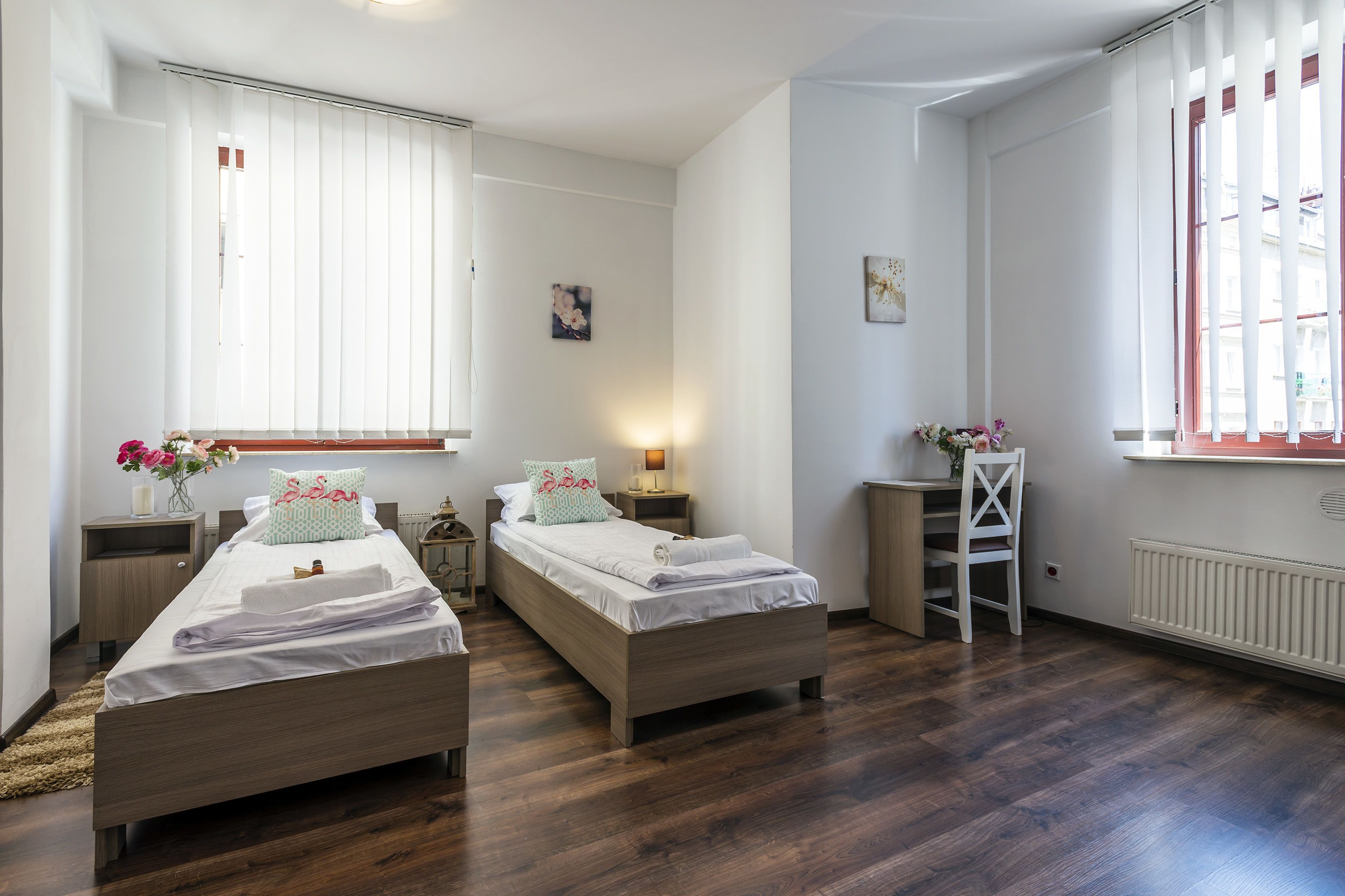 Une chambre avec deux lits simples, une table de chevet, une chaise et une fenêtre avec des stores.