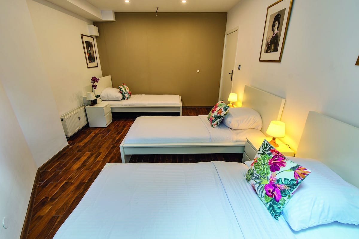 A hotel room with two single beds, a nightstand with a lamp, a radiator, and a framed picture on the wall.