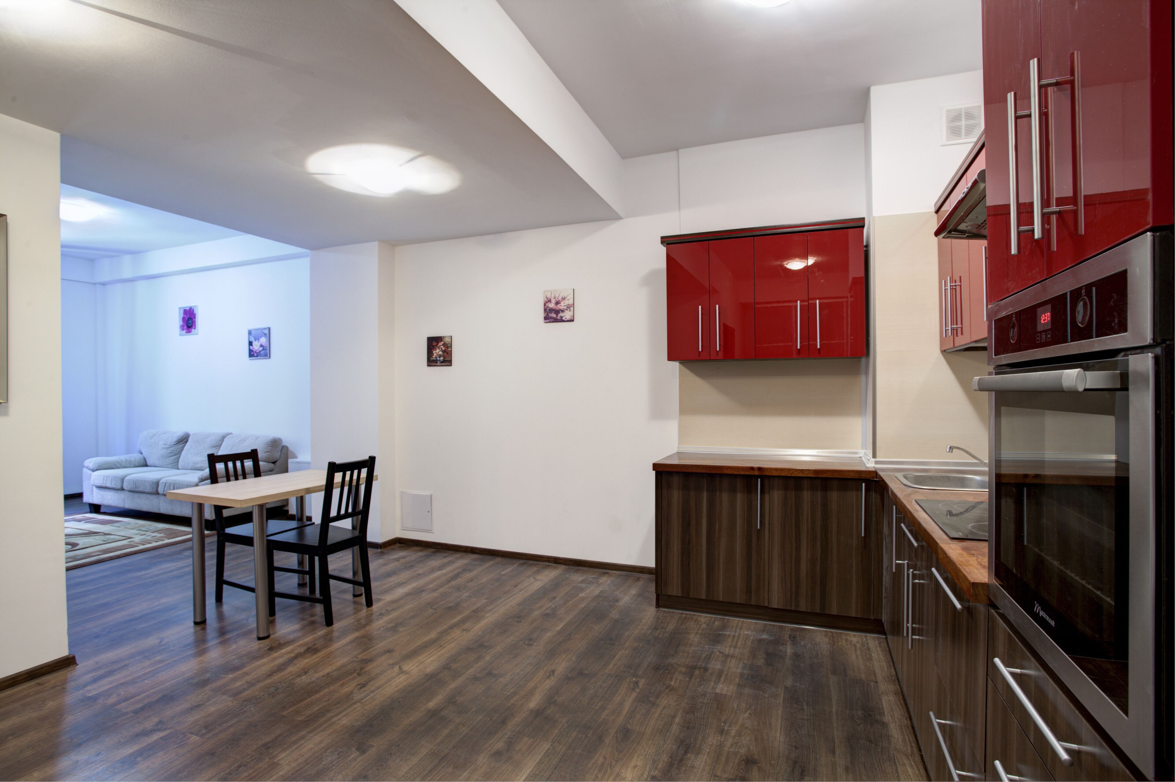 A modern kitchen with red cabinets, a stainless steel refrigerator, and a wooden dining table with chairs.