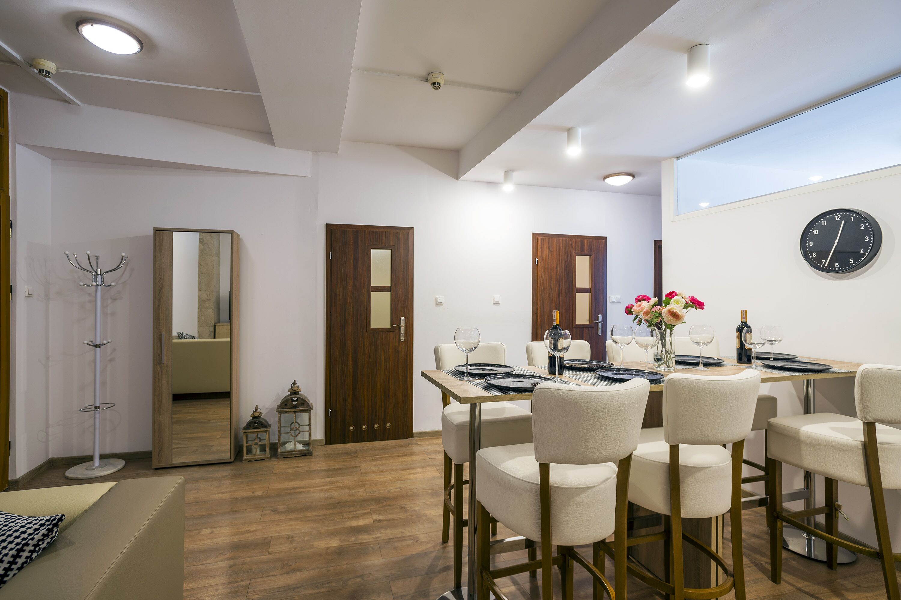 A dining area with a wooden table, white chairs, and a wall clock.