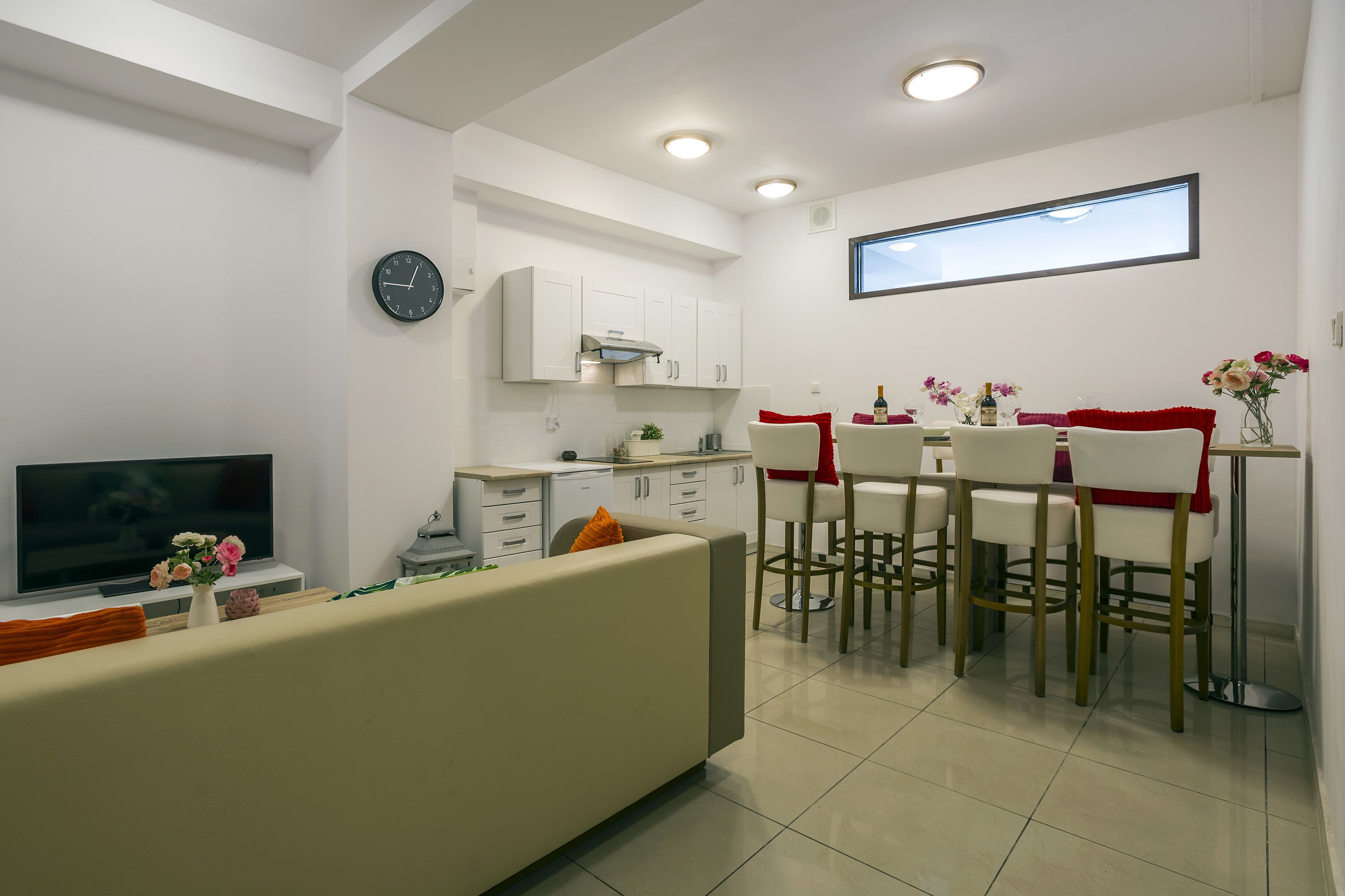 A modern living room with a sofa, TV, and a dining area with chairs and a table.