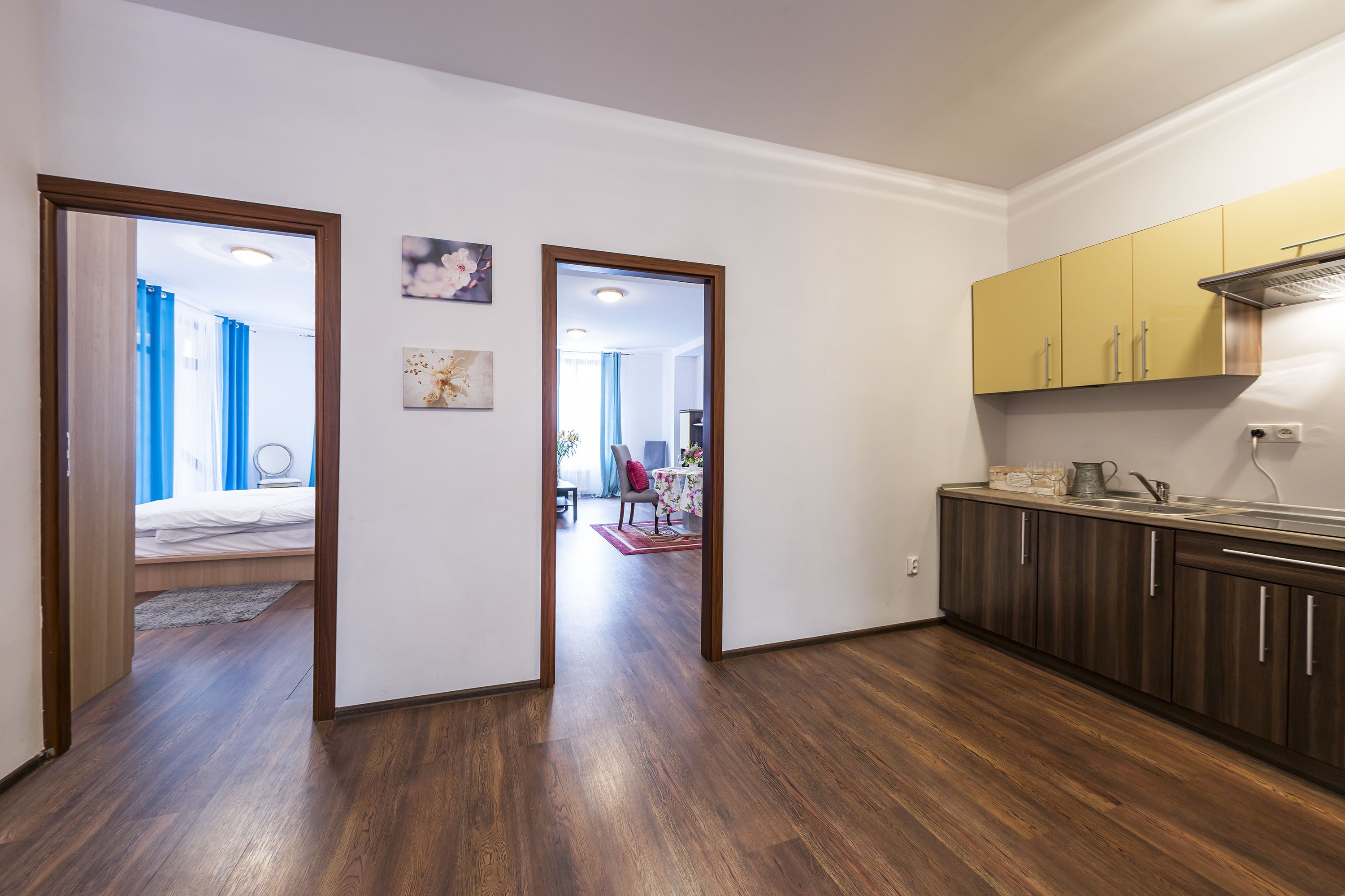 A modern kitchen with wooden cabinets and a dining area visible through an open door.