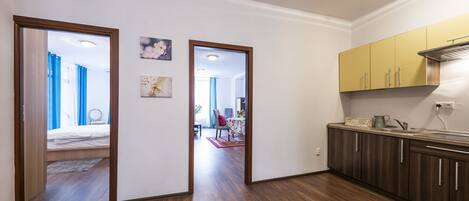 A modern kitchen with wooden cabinets and a dining area visible through an open door.