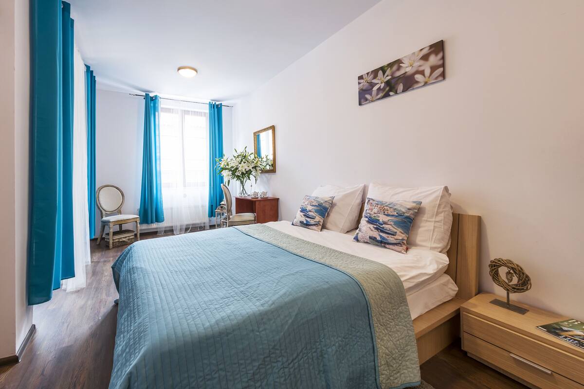 A bedroom with a bed, a nightstand, a chair, and a window with curtains.