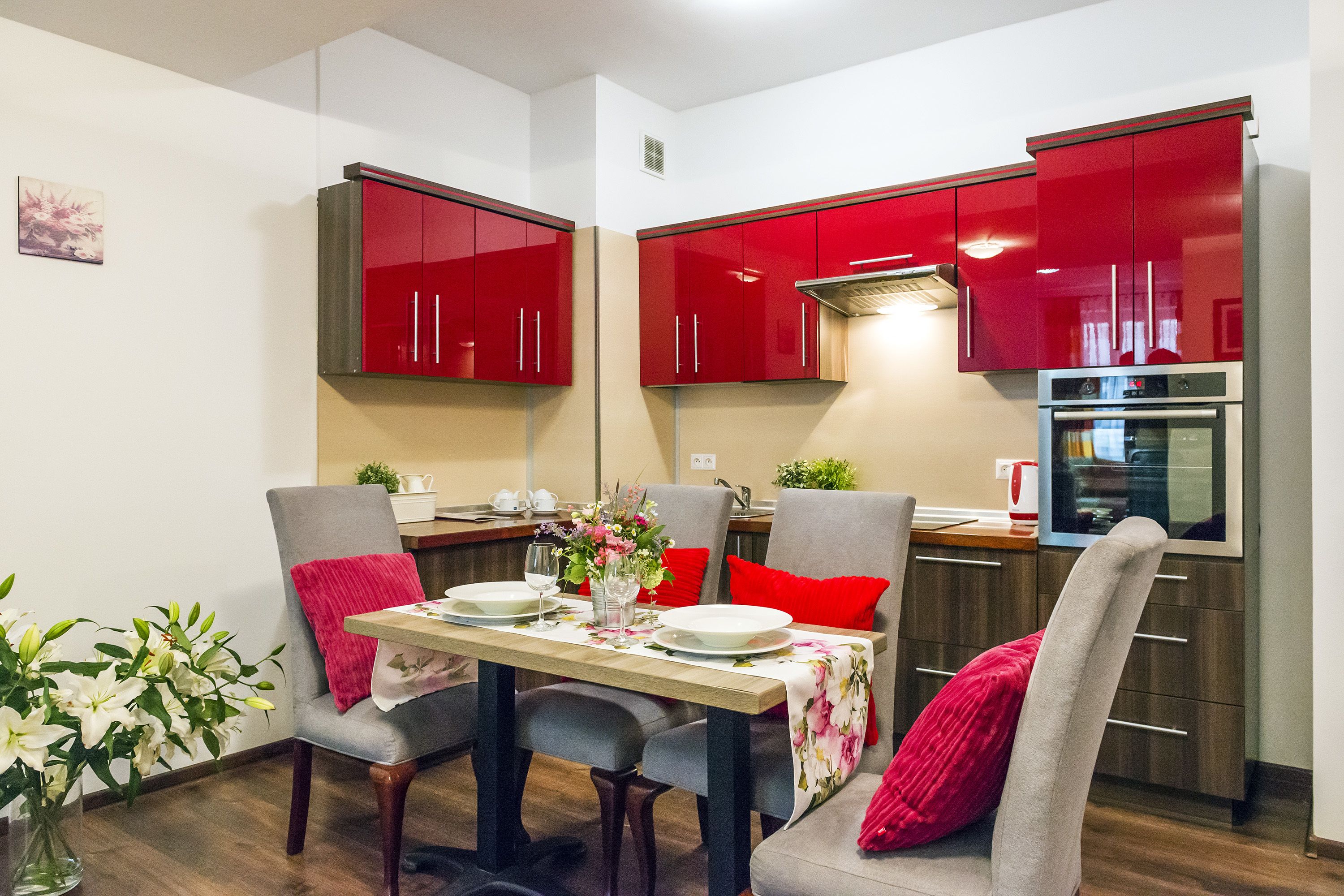 Una cocina moderna con armarios rojos, una mesa de comedor para dos personas y un horno empotrado.