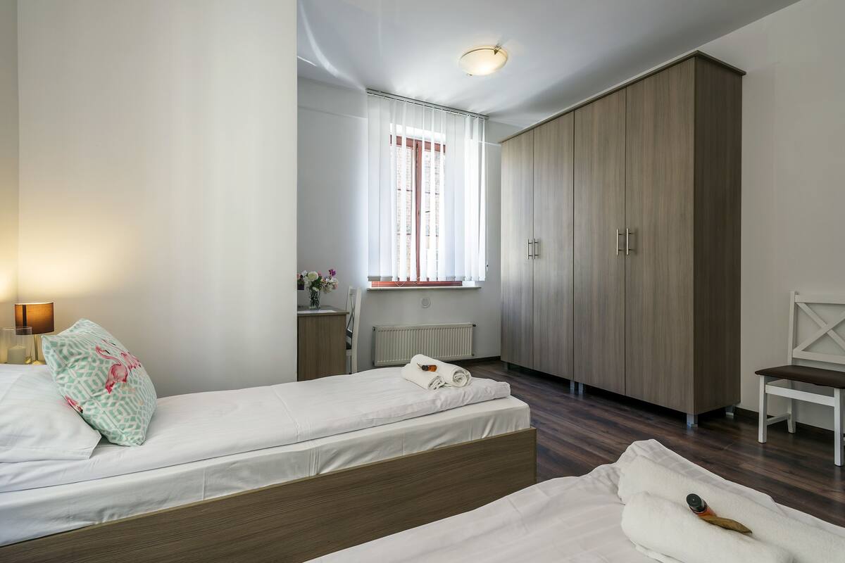 A bedroom with two beds, a wardrobe, a radiator, and a window with curtains.