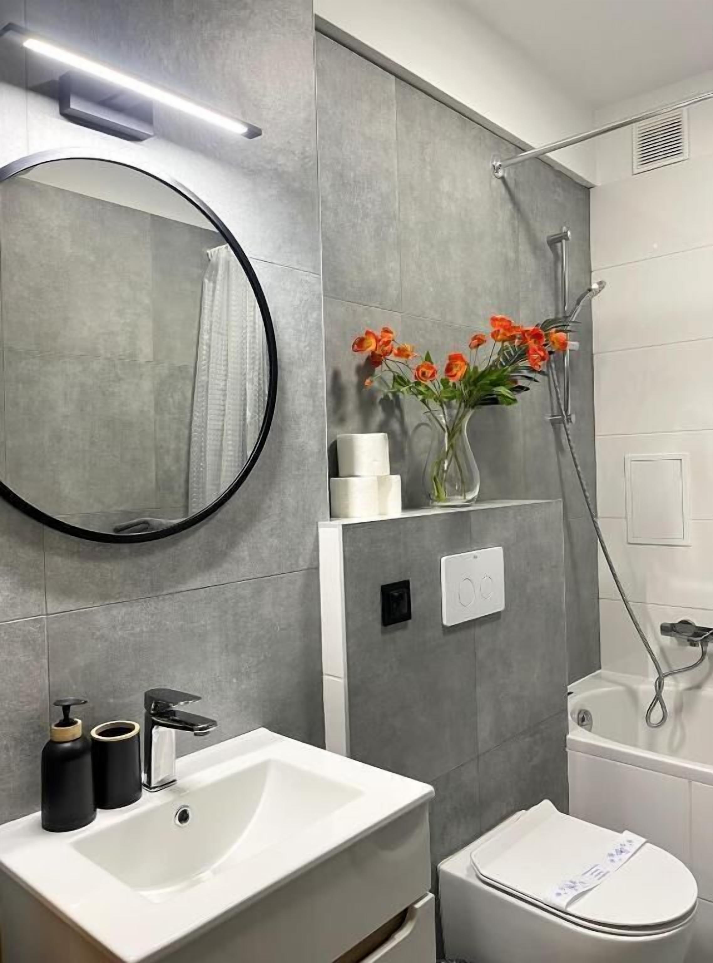A modern bathroom with a white sink, a round mirror, a toilet, and a shower.