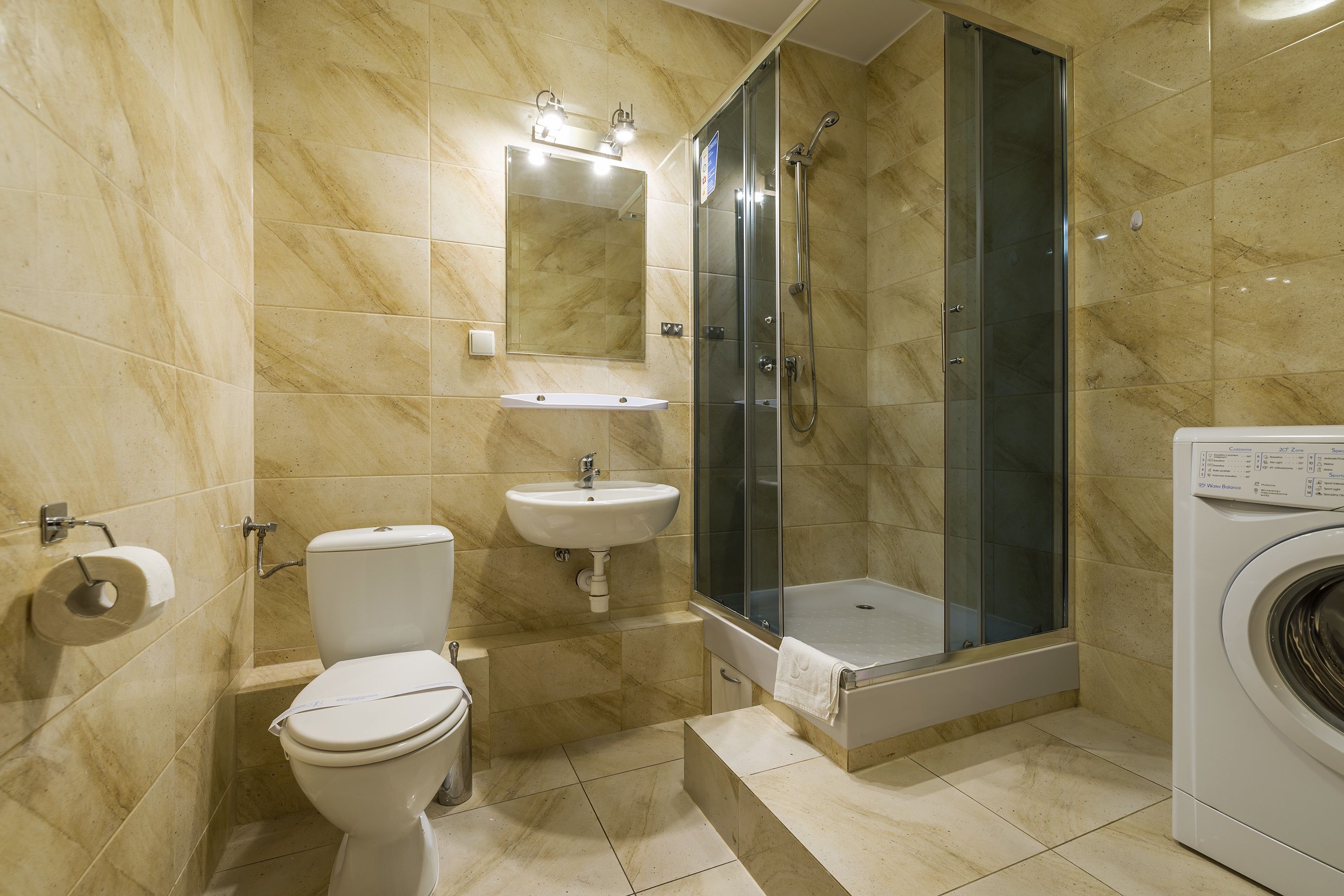 A bathroom with a toilet, sink, shower, and washing machine.