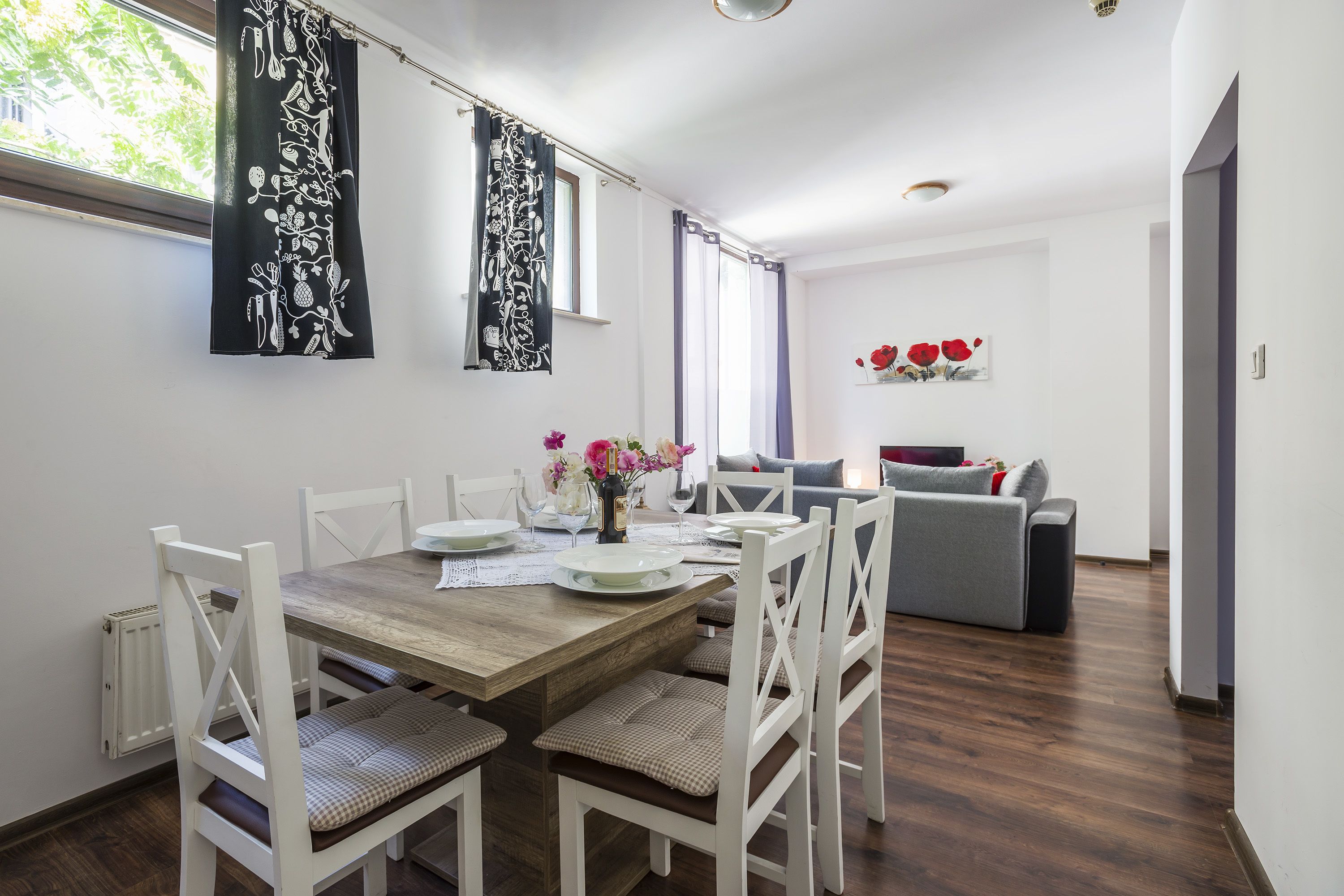 A dining area with a wooden table, white chairs, and a vase of flowers.