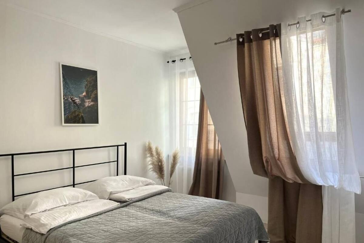 A bedroom with a bed, curtains, a painting, and a window.
