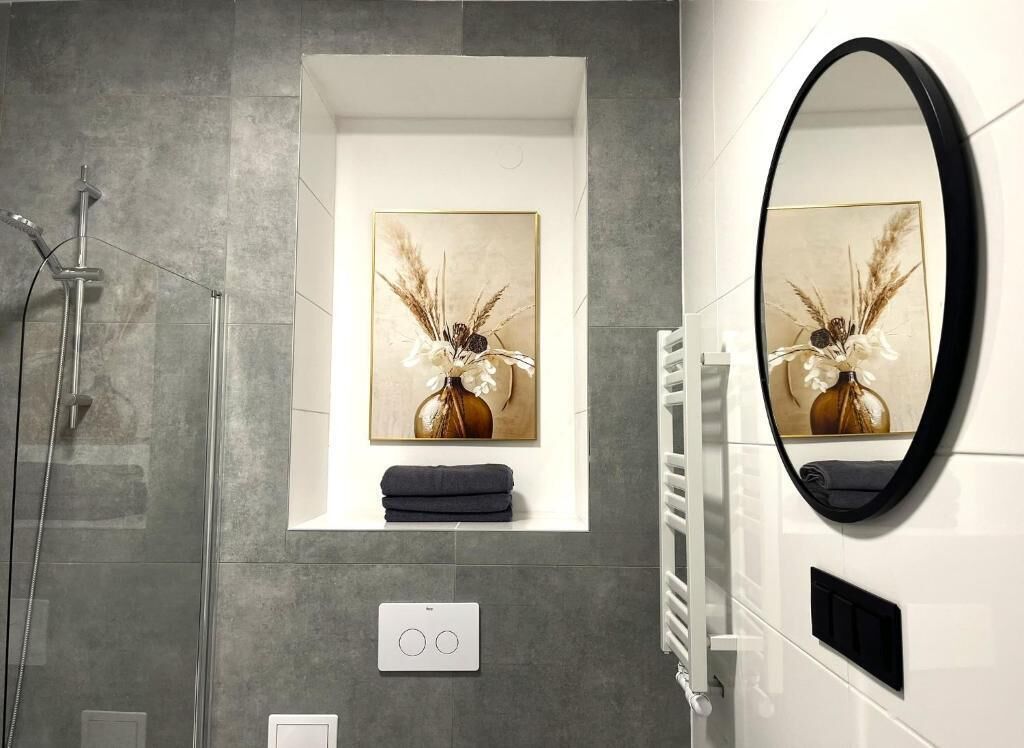 Een moderne badkamer met een douche, een ingelijste afbeelding, een handdoek, een thermostaat en een spiegel.
