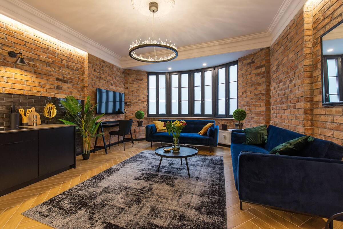 A modern living room with a brick wall, a blue sofa, a coffee table, and a chandelier.
