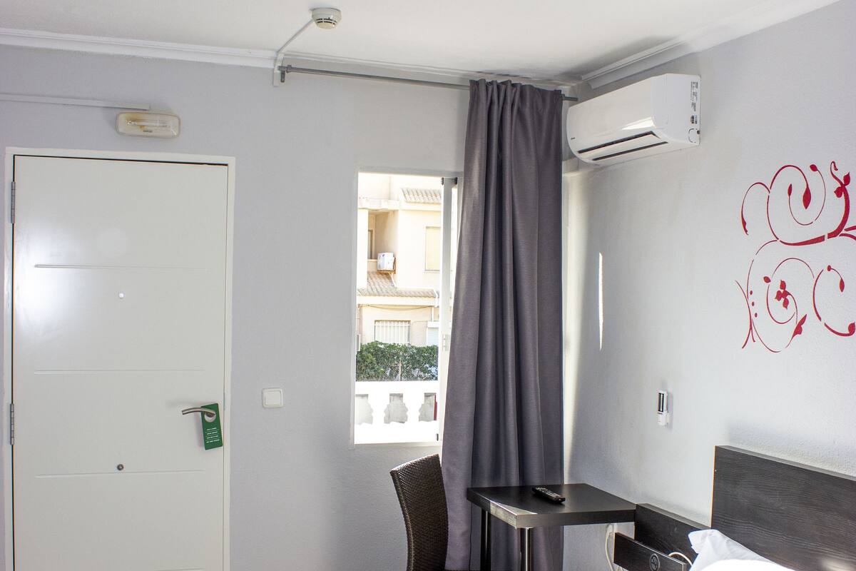 Ein Hotelzimmer mit Bett, Schreibtisch, Stuhl, Klimaanlage, einem Fenster mit Vorhängen und einer Tür.