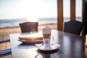 A table with a cup of coffee and a plate of food, with a view of the beach in the background. - Hostal Alba (Torrevieja)