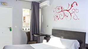 Habitación de hotel con cama, una silla, una mesa y ventana con vista a edificios.