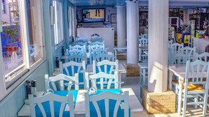 Un restaurante con sillas y mesas blancas, manteles azules y copas de vino sobre las mesas.