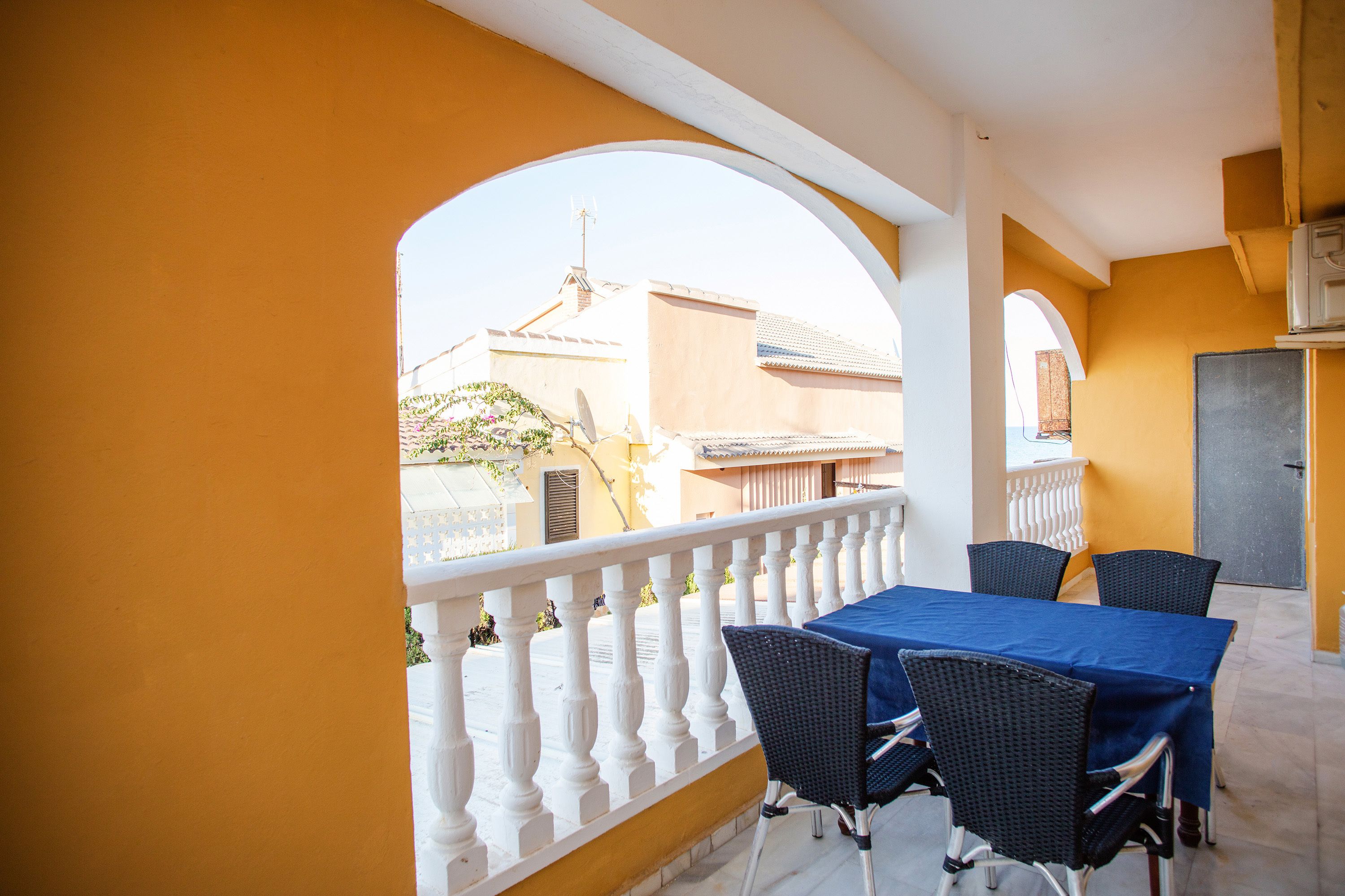 En balkong med ett vitt räcke, ett blått bord och fyra fåtöljer i rotting.