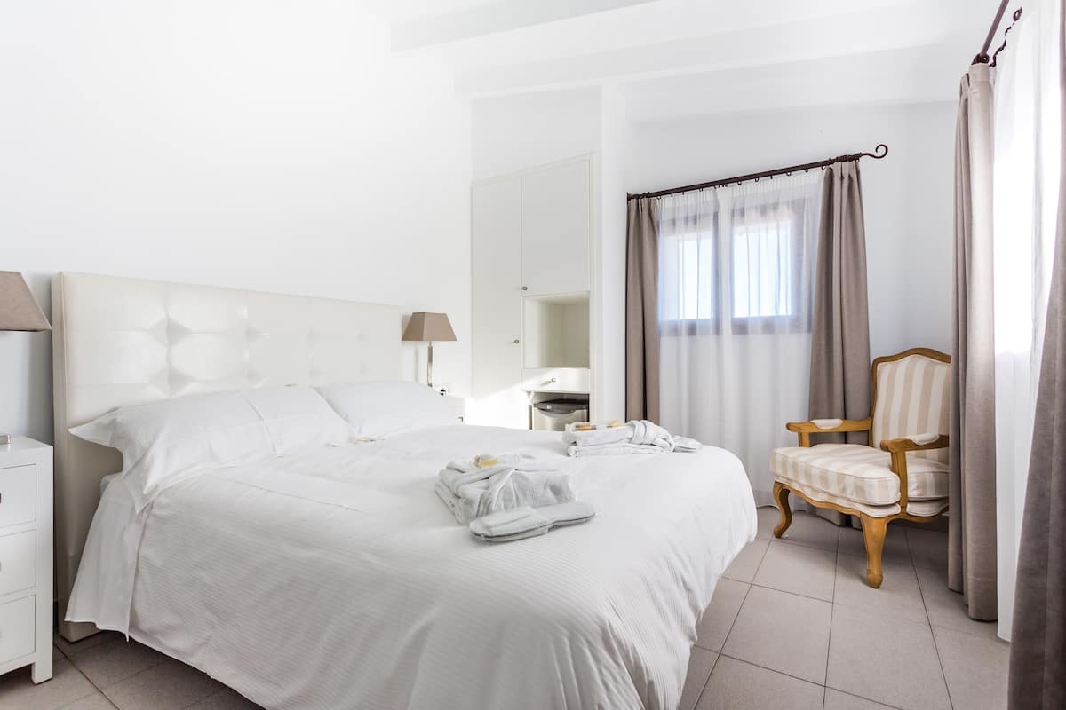 Een hotelkamer met een groot bed, een houten stoel, een nachtkastje en een spiegel.