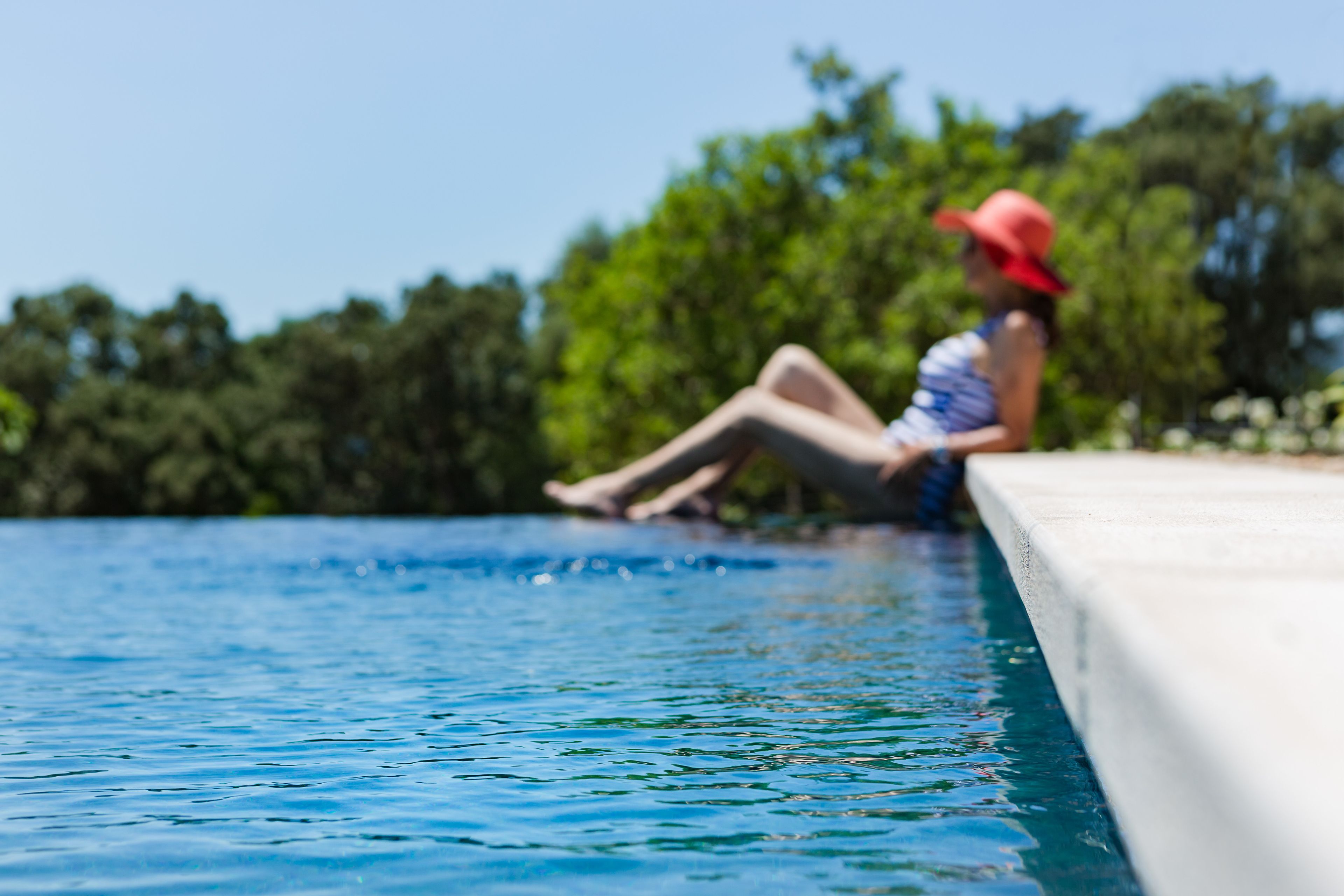 A person sitting by a pool with a clear view of the water and greenery in the background.
