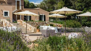 A building with outdoor seating and umbrellas, surrounded by greenery and steps leading to a door. - Agroturismo Ses Vistes (Porreres)