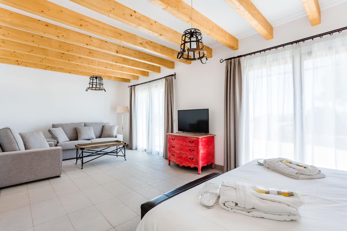 Een hotelkamer met een bed, een bank, een televisie, een rode dressoir en een houten plafond.