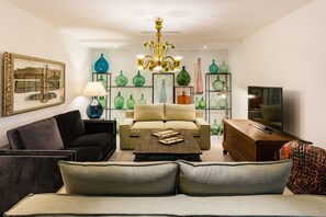 Un salon comprenant un canapé, une table basse, un téléviseur et des étagères ornées de vases décoratifs.