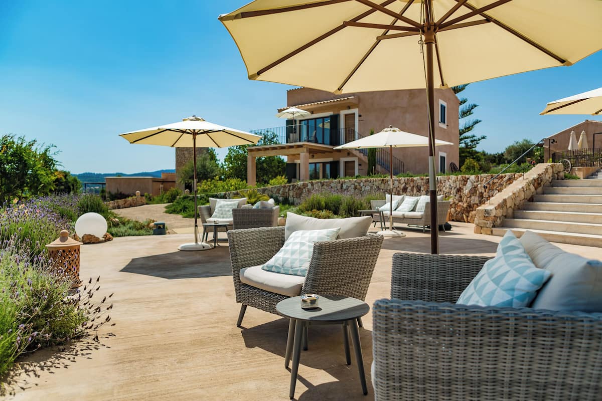 Een terras met rieten meubilair, parasols en een stenen muur.