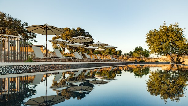 A serene poolside area with lounge chairs and umbrellas, reflecting on the water. - Agroturismo Ses Vistes (Porreres)