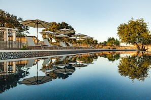 Ein ruhiger Poolbereich mit Liegestühlen und Sonnenschirmen, deren Spiegelung sich im Wasser zeigt.