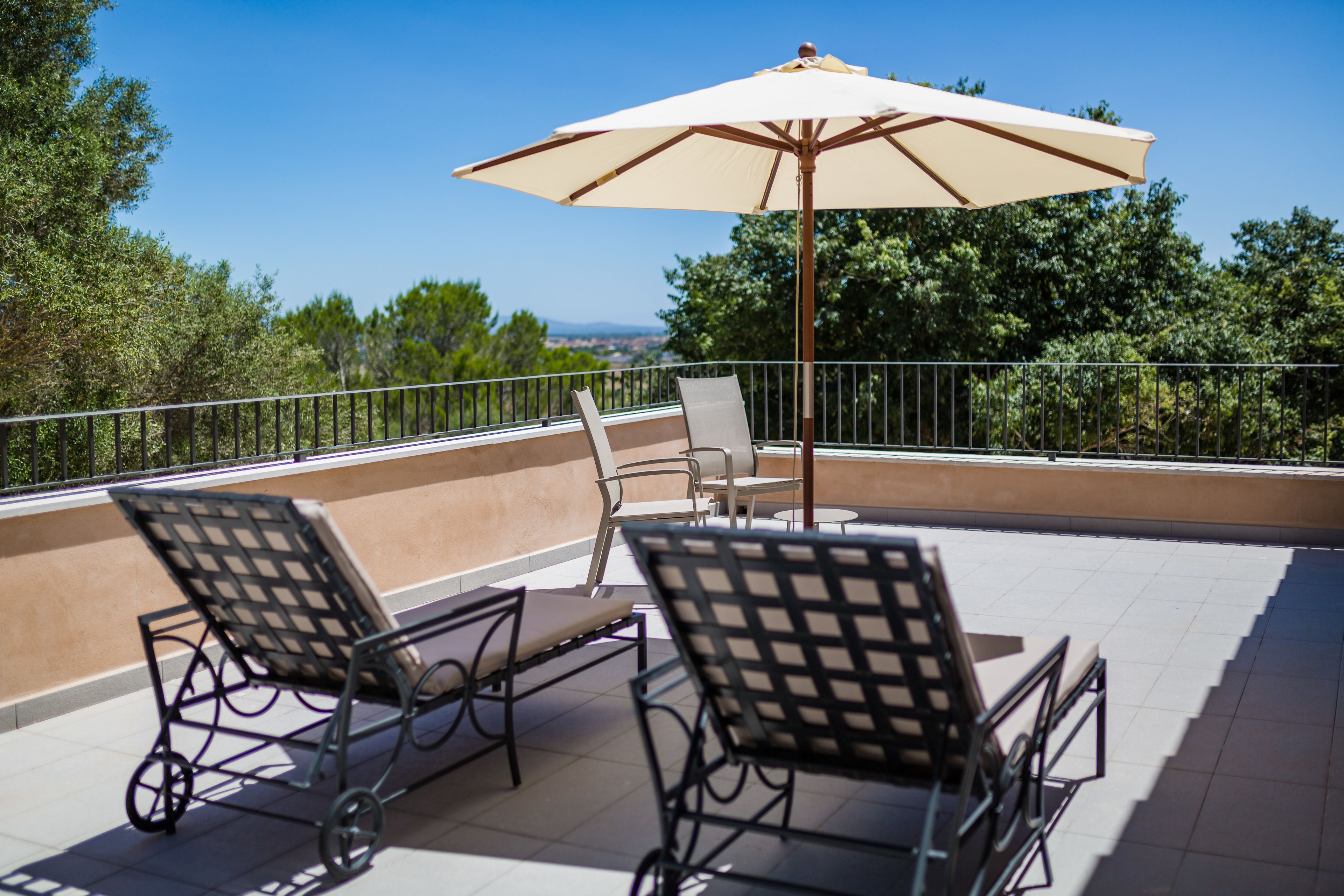 Une terrasse avec deux chaises en métal et un grand parasol, offrant une vue panoramique sur un paysage verdoyant avec des arbres et des collines à l’horizon.