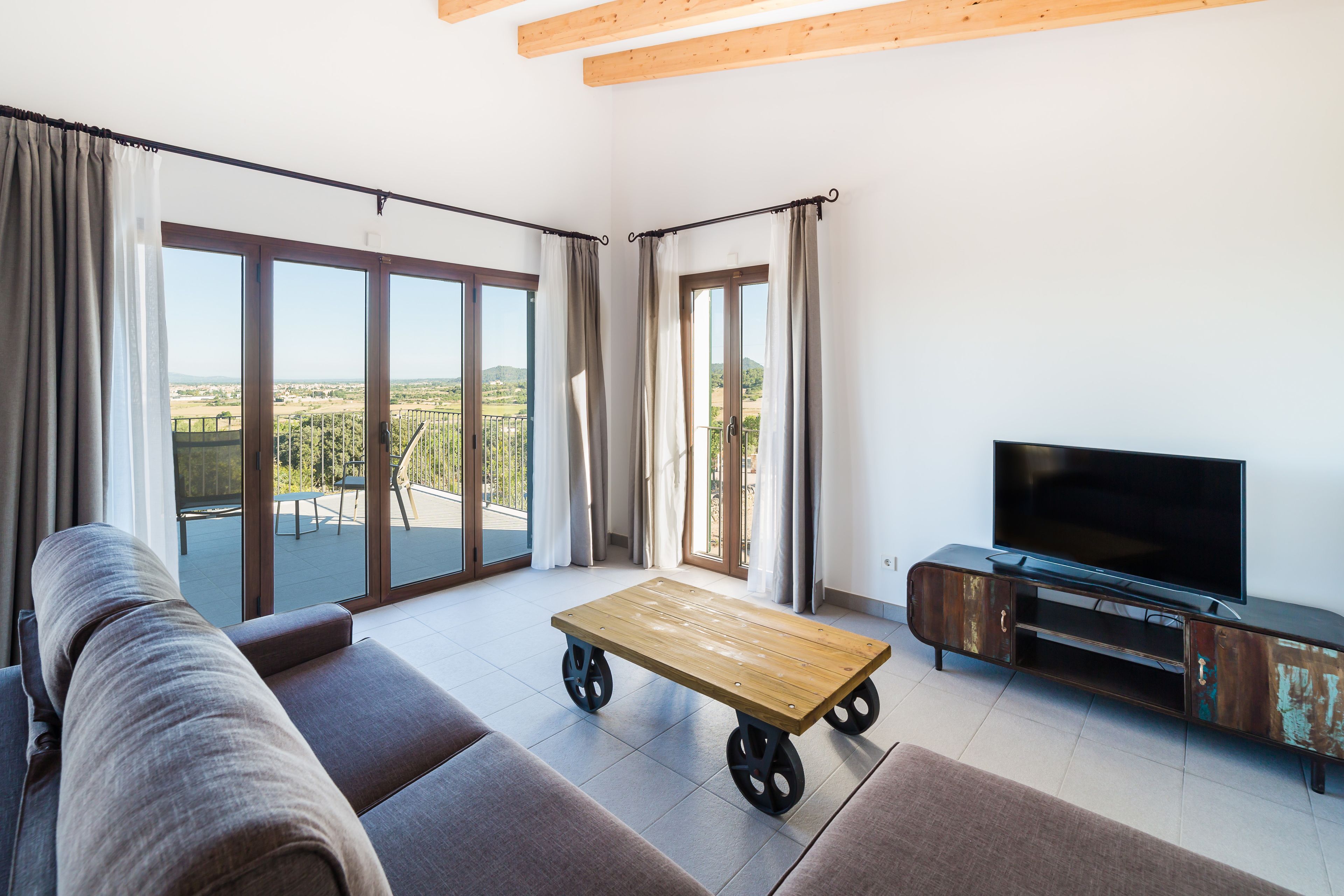 Una sala de estar moderna con un sofá, una mesa de centro de madera con ruedas, un televisor sobre un mueble de madera y grandes puertas correderas de vidrio que dan a un patio exterior.