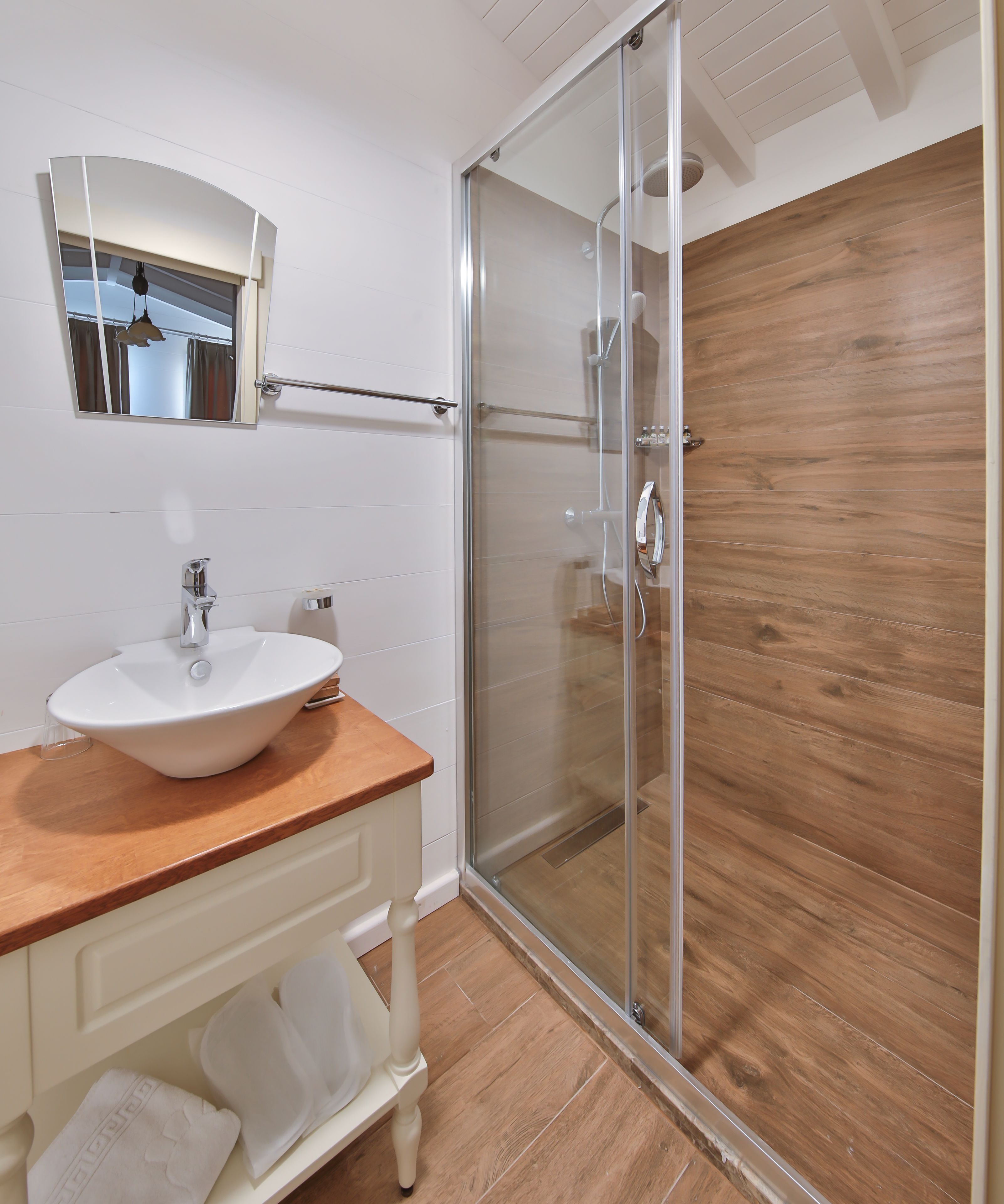 A modern bathroom with a white sink, wooden countertop, and a glass shower enclosure.